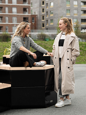 Two girls sitting together on a Rosenlund seating group having a conversation.